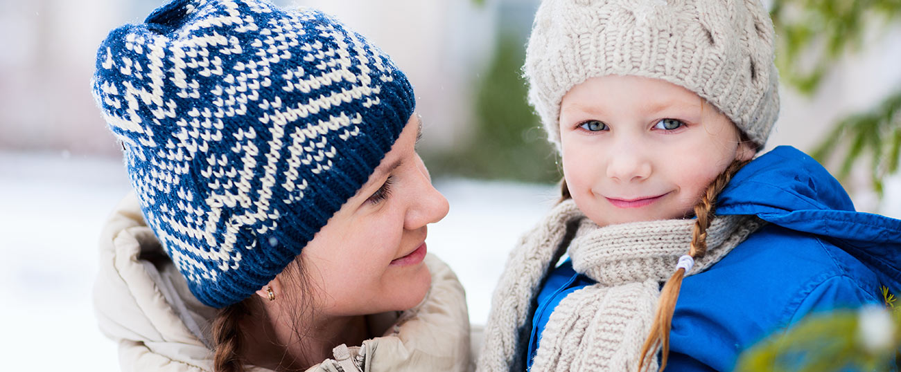 Bambina con cappello, sciarpa e trecce e mamma in inverno nel Plan de Corones