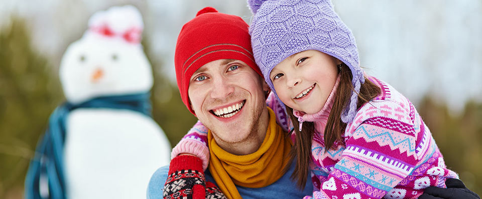 Vater und Tochter lächelnd mit Schneemann im Hintergrund