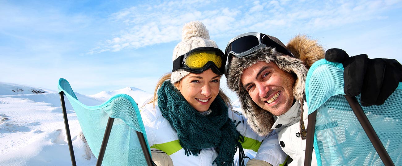 Mann und Frau in Skibekleidung sitzen auf zwei Stühlen mitten im Schnee