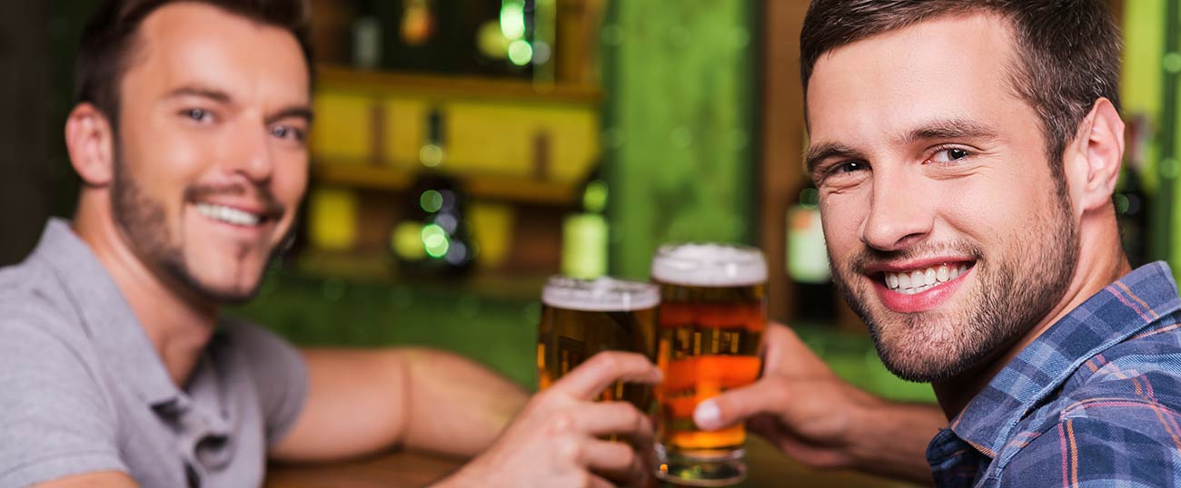 Due uomini brindano in un pub con un bicchiere di birra e guardano nell'obiettivo